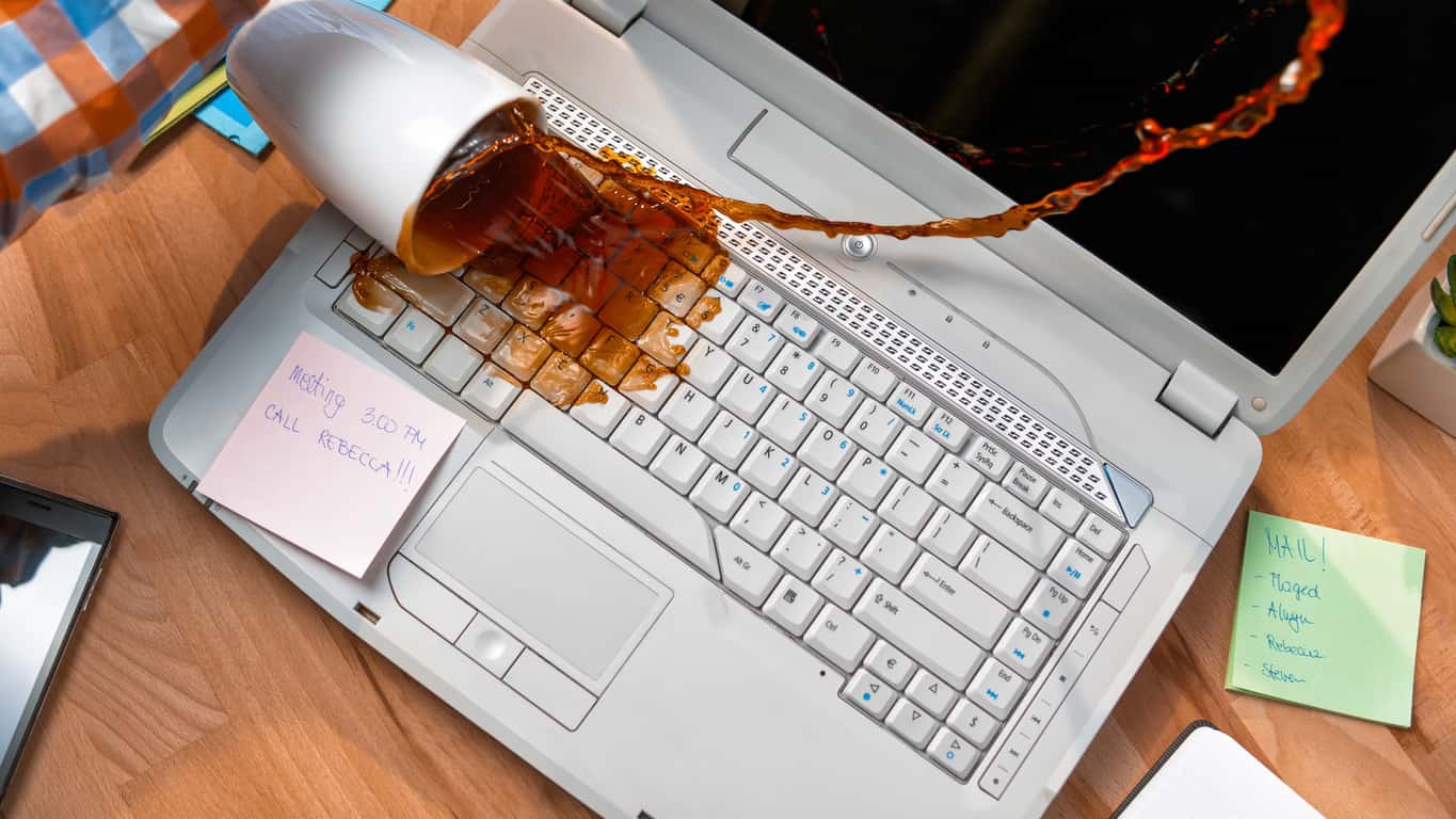 A laptop on a wooden table with coffee spilled on the keyboard signifies the employee needs more than homeowners insurance to cover the loss