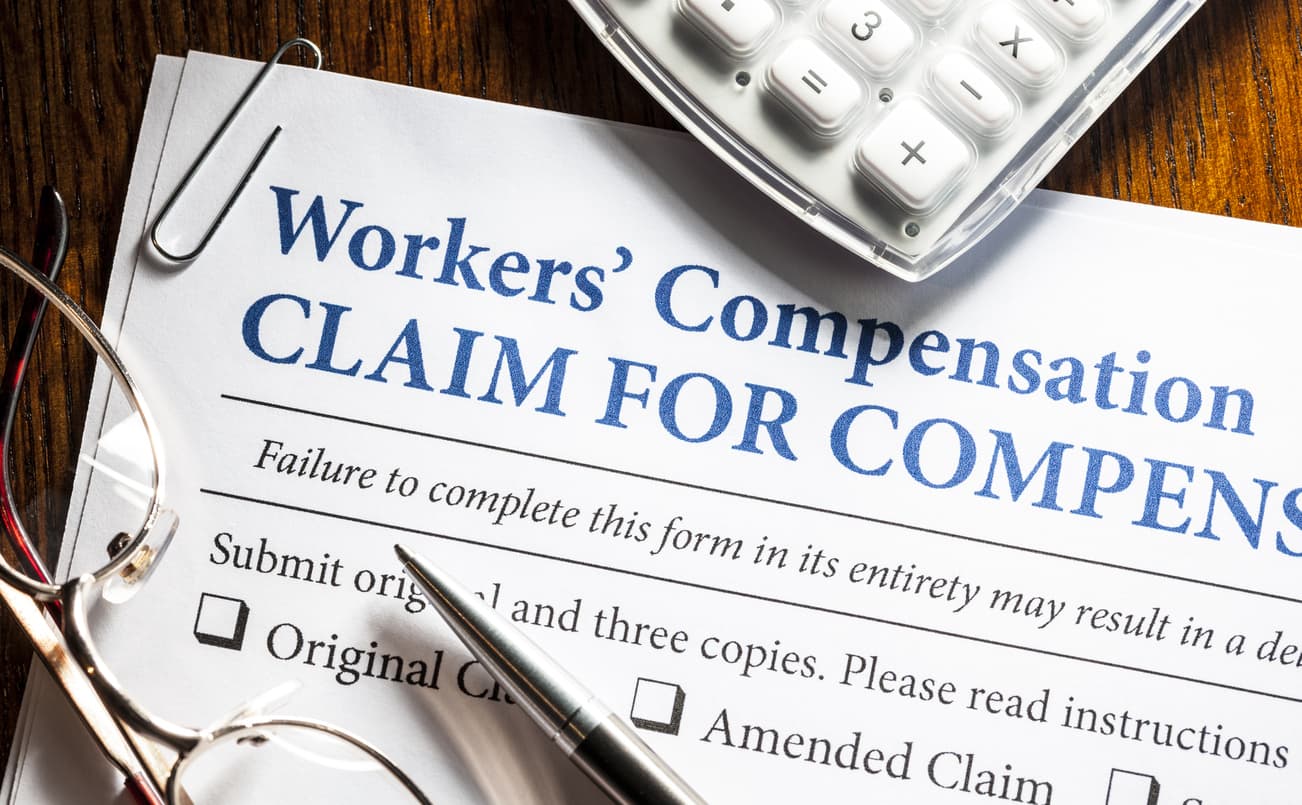 A workers’ comp insurance form on a desk with a calculator and glasses