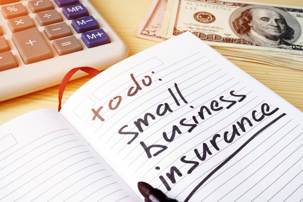 A notebook, calculator, and money on a desk signify wanting to save money on business insurance